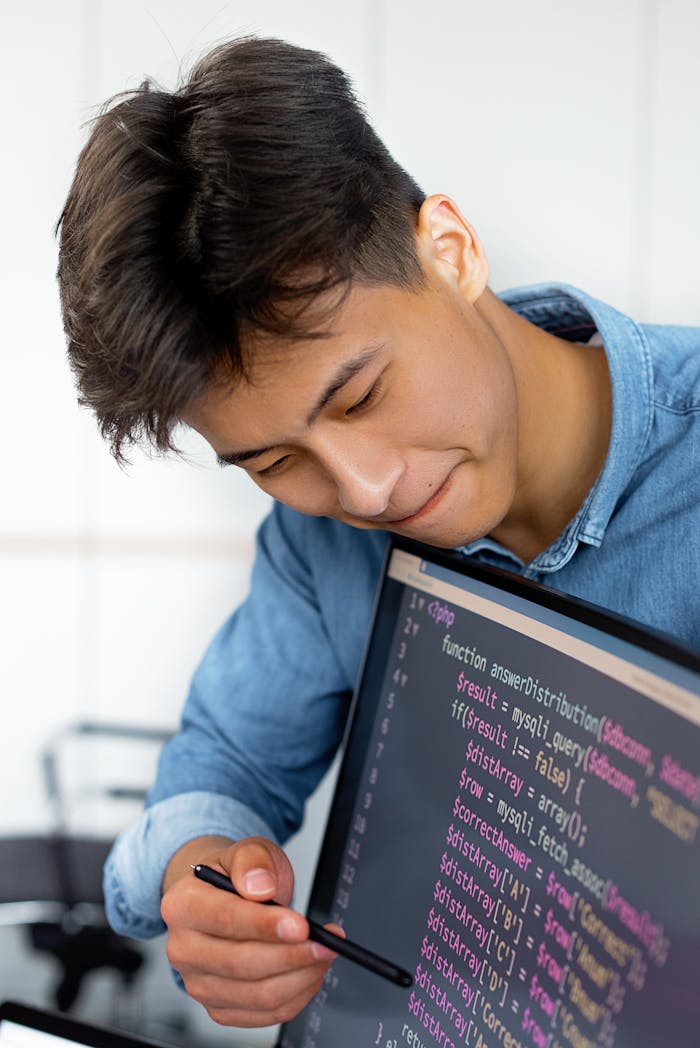 A young man smiles while programming in a modern office environment.
